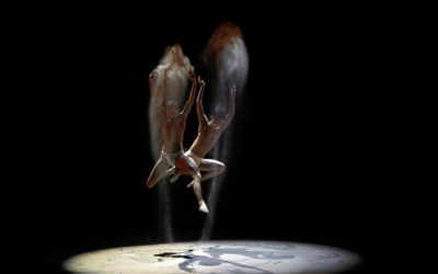 Two dancers jump in the air throwing sand